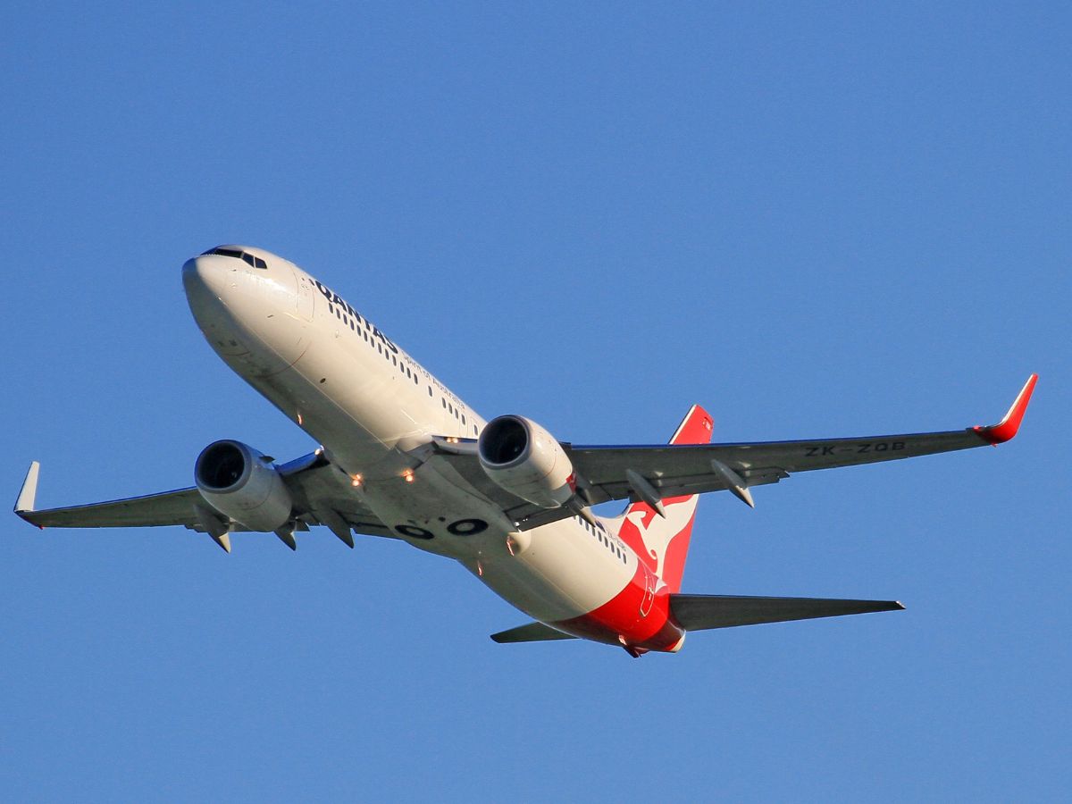 Qantas plane in flight with a light blue sky background.